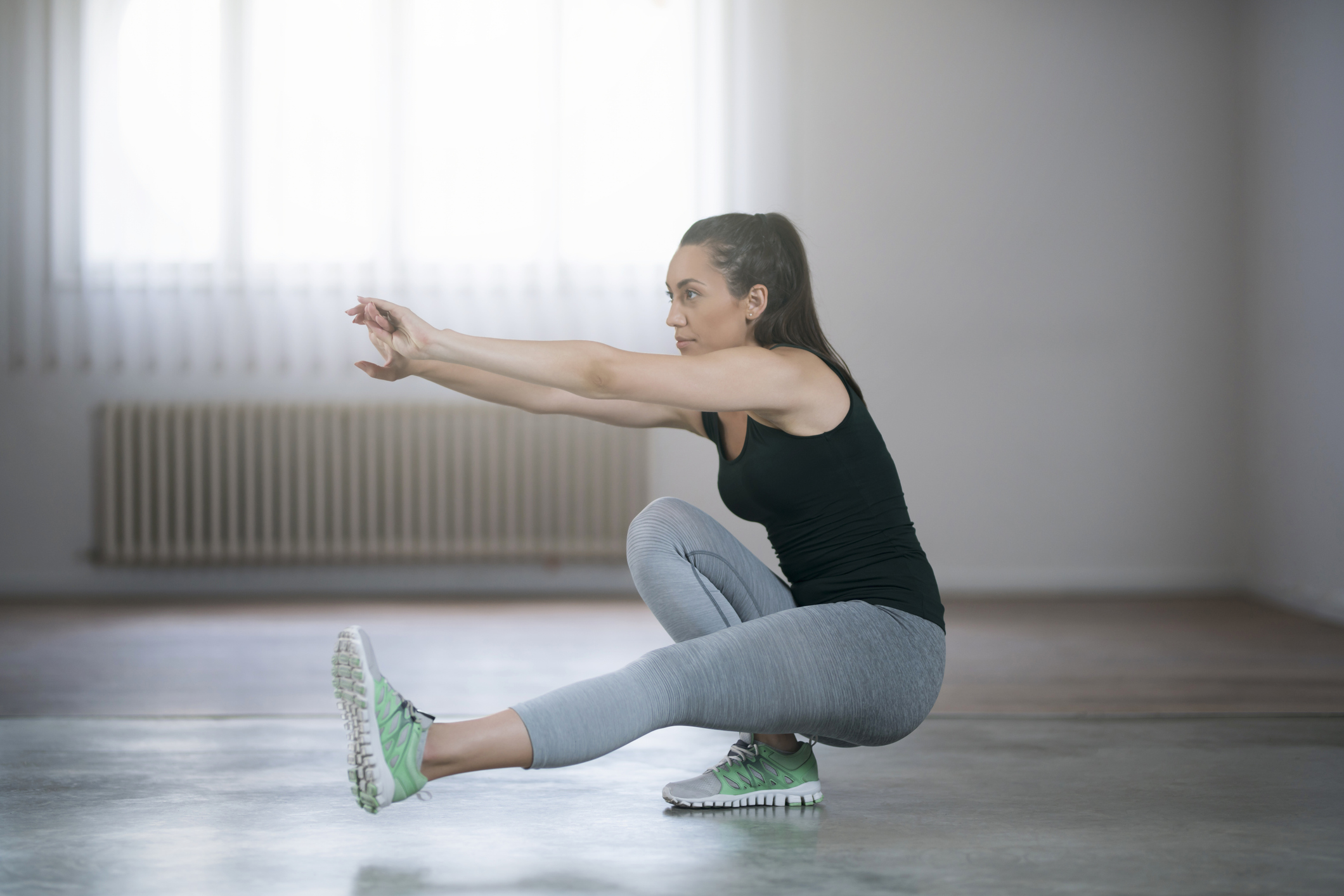 female trainer with a ponytail demonstrates a single-leg step down as the first part of a pistol squat progression